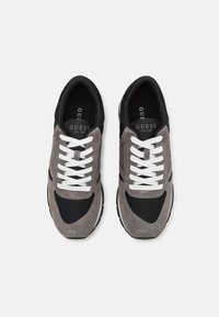 Sneaker in suede grigio e mesh nero con lacci bianchi, caratterizzati da una punta arrotondata e un pannello laterale testurizzato con dettagli del marchio.