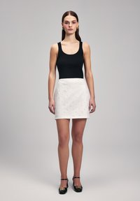 Débardeur noir à côtes et jupe mini en dentelle blanche, avec une silhouette ajustée. Des chaussures à talons noires avec des accents dorés complètent la tenue.