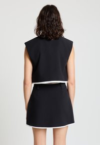 Schwarzes ärmelloses bauchfreies Oberteil mit weißer Borte, kombiniert mit einem schwarzen Minirock mit glatter Textur und klaren Linien.