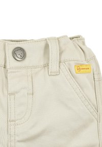 Beige broek van katoen met een gladde textuur, voorzien van een metalen knoop in de vorm van een beer, een gele merkteken en standaardzakken.