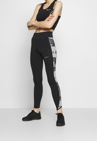 Czarny sportowy stanik i czarne legginsy z graficznym czarno-białym panelem po boku. Legginsy mają wysoki stan i dopasowany fason.