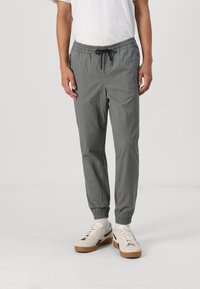 Grå avsmalnande joggers i lätt tyg med elastisk midja, snörning och elastiska muddar, kombinerat med beige sneakers.