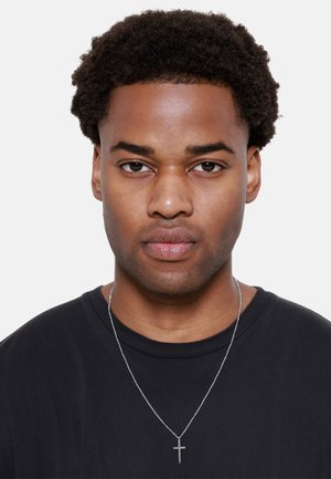 Male figure wearing a black T-shirt, featuring short curly hair. A silver chain necklace with a cross pendant is visible.