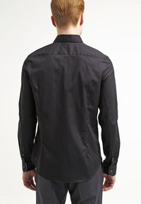 Camicia nera a maniche lunghe con una texture del tessuto liscia, colletto a punta e polsini con bottoni. Design aderente con orlo curvo sul retro.