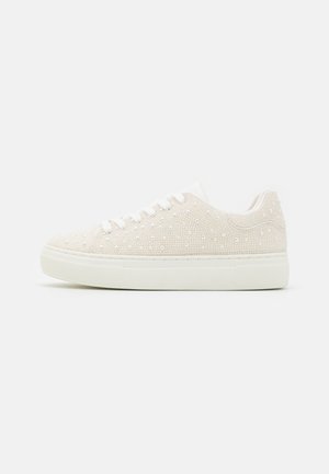 Beige sneakers with textured surface, adorned with small white beads, flat white rubber sole, and lace-up design. Simple, rounded shape.