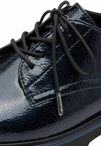 Scarpa in vernice nera con una superficie liscia e lucida, punta rotonda e lacci neri con un accento metallico sulla punta dei lacci.