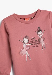 Sudadera rosa con cuello acanalado, que presenta dos bailarinas de dibujos animados y acentos brillantes, y el texto: "NO te rindas, cuanto más practiques, mejor lo harás."