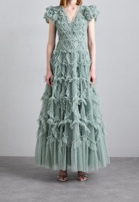 Robe longue vert clair composée de tissus superposés et à volants, avec un col en V et des accents texturés. Comprend un matériau transparent à pois.