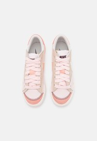 Nike-sneakers med en rosa läderöverdel med sydda detaljer, ljusrosa snören och en strukturerad sula. Klassisk design med subtil färgvariation.