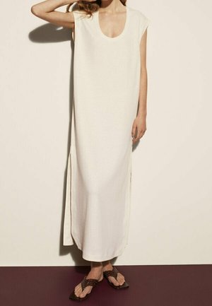 Abito lungo bianco senza maniche con scollo rotondo, spacchi laterali, realizzato in tessuto leggero, abbinato a sandali marroni con cinturini.