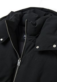Giacca a vento nera con colletto alto, chiusura con zip e bottoni a pressione. Caratterizzata da ricamo "Utopia" e una fodera interna morbida e texture.