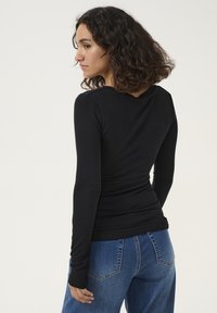 Maglietta nera a maniche lunghe con un design aderente, texture liscia e scollo a V, abbinata a jeans larghi blu con tasche posteriori.