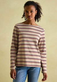 Beige Langarmshirt mit horizontalen Streifen in Burgunder und Marineblau. Rundhalsausschnitt und lockere Passform. Getragen über blauen Jeans.