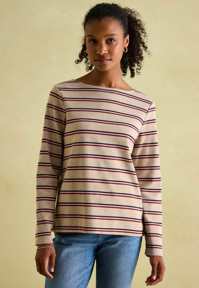 Beige Langarmshirt mit horizontalen Streifen in Burgunder und Marineblau. Rundhalsausschnitt und lockere Passform. Getragen über blauen Jeans.