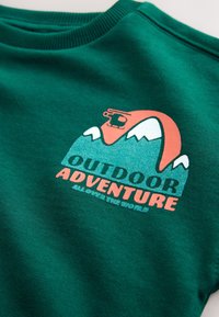 Sweat-shirt vert avec un graphique de montagne, un hélicoptère au-dessus et le texte « Outdoor Adventure Always The World. »