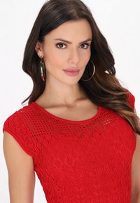 Vestito rosso lavorato a maglia con maniche corte, caratterizzato da un motivo testurizzato simile a pizzo e un collo rotondo, indossato con grandi orecchini a cerchio.