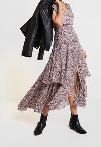 Sukienka w cętki w kolorze różowym i kremowym, z rozkloszowanym dołem i wysokim rozcięciem, w połączeniu z czarną skórzaną kurtką i botkami za kostkę.