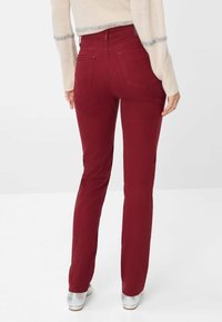 Jeans dritti color bordeaux con vita media, dotati di due tasche posteriori e una trama del tessuto liscia, abbinati a scarpe argentate.