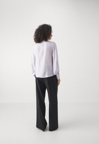 Light purple long-sleeve blouse with a textured pattern and a round neckline, paired with black wide-leg trousers.