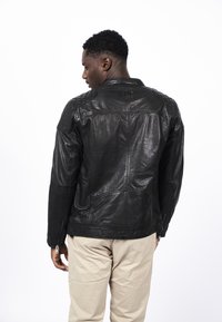 Černá kožená bunda s prošívanými ramenními akcenty, švem na zadní části a zipovými manžetami. Hladká textura, přiléhavý střih.