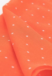 Tessuto arancione con pois bianchi, caratterizzato da una texture morbida e pieghe drappeggiate, che mette in risalto un aspetto leggero e liscio.