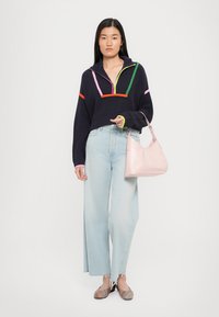 Marineblauwe cropped sweater met kleurrijke strepen, lichtblauwe wijde jeans en een roze handtas. Het schoeisel heeft een gestreept ontwerp.
