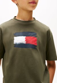 Olivgrön bomull t-shirt med ett målat rektangeldesign i vitt, rött och marinblått. Rund halsringning och korta ärmar.