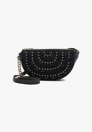 Bolso cruzado negro en forma de media luna con tachuelas doradas en patrones circulares, cierre de cremallera y una correa de cuero con detalle de eslabón de cadena dorada.