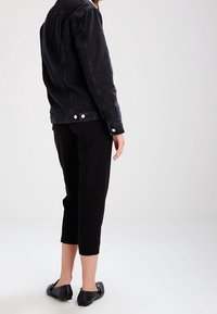 Svart denimjacka med klassisk skärning, tillsammans med avklippta svarta byxor och platta svarta skor. Denna outfit har minimalistiska designelement.