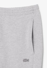 Pantalones de chándal grises claros hechos de un material suave, con una cintura ajustable mediante cordón y un detalle de logo bordado en el lateral.