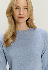 Jasnoniebieski sweter dzianinowy z okrągłym dekoltem i rękawami raglanowymi, charakteryzujący się miękką teksturą i minimalistycznym wzornictwem.