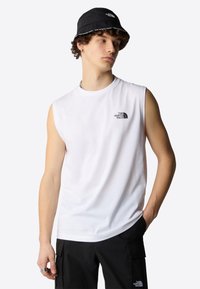Hvit ermeløs t-skjorte med svart logo, kombinert med svarte cargo-bukser. Svart bøttehatt med logotrim. Enkelt, sporty design.