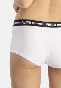 Boxers cortos de algodón blanco con una cinturilla elástica negra que lleva el logo de PUMA y rayas azules en contraste. Textura suave.