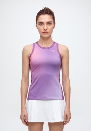 Une femme porte un haut de sport violet sans manches et une jupe de tennis blanche sur un fond clair uni.