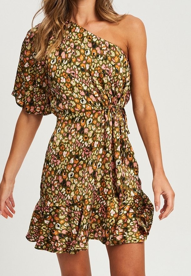 Femme portant une robe courte fleurie asymétrique avec un ourlet à volants et une taille cintrée, en olive, rose, orange et blanc.