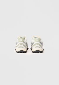 Gai pelēki un balti New Balance skriešanas apavi, skatīti no mugurpuses uz vienkārša baltā fona.