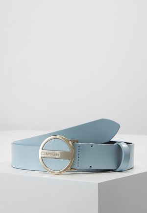 Lyseblåt læderbælte med en rund guldbeslag graveret med Calvin Klein-logoet, vist på en hvid overflade.