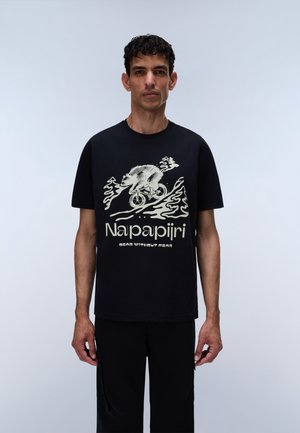 Homme portant un t-shirt noir avec un dessin blanc représentant un ours à vélo sur des vagues, texte « Napapijri » et « Bear Without Fear » en dessous.