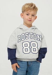 Szara bluza z krótkim rękawem i granatowymi akcentami, z napisem "BOSTON 88" wydrukowanym na biało. Miękka tkanina, luźny krój, zestawiona z niebieskimi dżinsami.