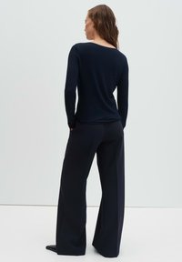 Marineblaues Langarmoberteil in taillierter Passform, kombiniert mit locker sitzenden marineblauen Hosen. Glatte Textur mit einer schlichten und klaren Silhouette.