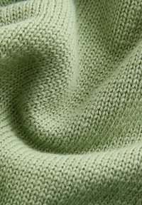 Hellgrüner Strickstoff mit einem strukturierten, gewebten Muster. Das Material wirkt weich und gemütlich und zeigt einen sanften, gedämpften Farbton.