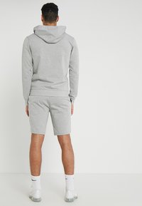 Sudadera de algodón gris con capucha ajustable, combinada con pantalones cortos gris a juego. Diseño sencillo, textura suave y dobladillos elásticos. Calcetines blancos y zapatillas deportivas.