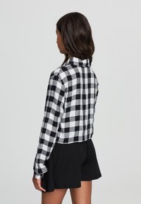 Camicia di flanella a quadretti bianco e nero con colletto, design corto e maniche lunghe, abbinata a pantaloni corti neri.