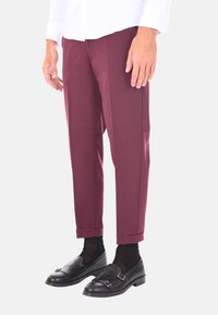 Pantaloni su misura color bordeaux con una texture liscia, gambe affusolate e orli risvoltati, abbinati a mocassini neri e calzini neri trasparenti.