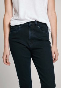 Tmavě modré džíny s vysokým pasem, klasickým designem pěti kapes, decentními detaily stehu a předním zapínáním na knoflík.