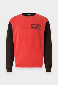 Duga crvena i smeđa majica dugih rukava s okruglim izrezom, s crnim grafičkim logotipom na prsištu. Izrađena od meke mješavine pamuka.