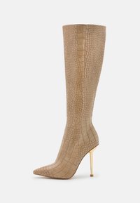 Botte beige montant jusqu'au genou avec une texture crocodile, bout pointu et talon stiletto doré. Matériau lisse et design élégant.
