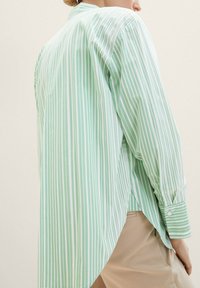 Helles grünes Langarmshirt mit weißen vertikalen Streifen, mit einem abgerundeten Saum und Knopfmanschette, aus einem glatten Stoff gefertigt.
