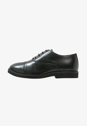 Czarny, elegancki oxford z skóry z nakładką na czubku, wiązany na sznurowadła, niski, ułożony obcas.