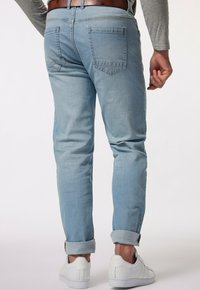 Vaaleansiniset farkut kapeutuvan lahkeen suunnittelulla, käärittyinä lahkeet, ja kaksi takataskua, yhdistettyinä valkoisiin urheilujalkineisiin.